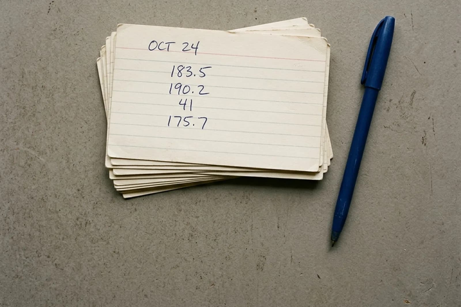 A stack of handwritten index cards and a pen on a grey surface.